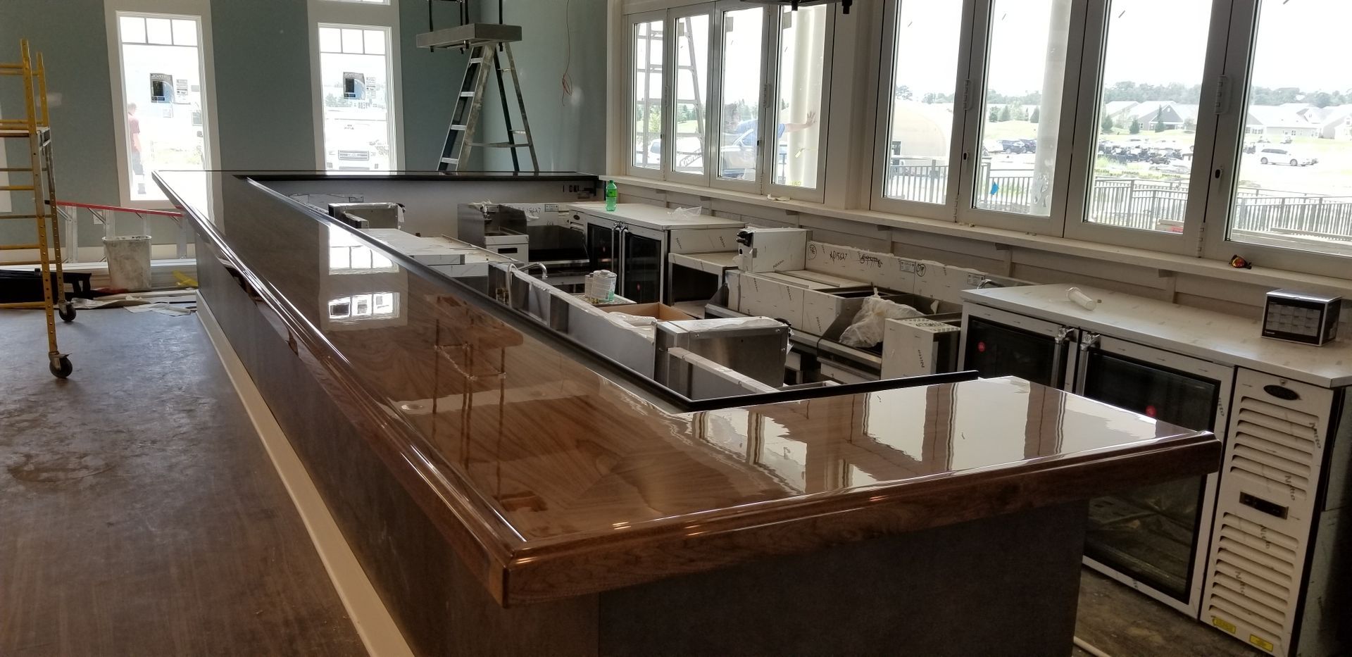 A bar with a shiny wooden countertop and stainless steel equipment, likely in a commercial setting with large windows.