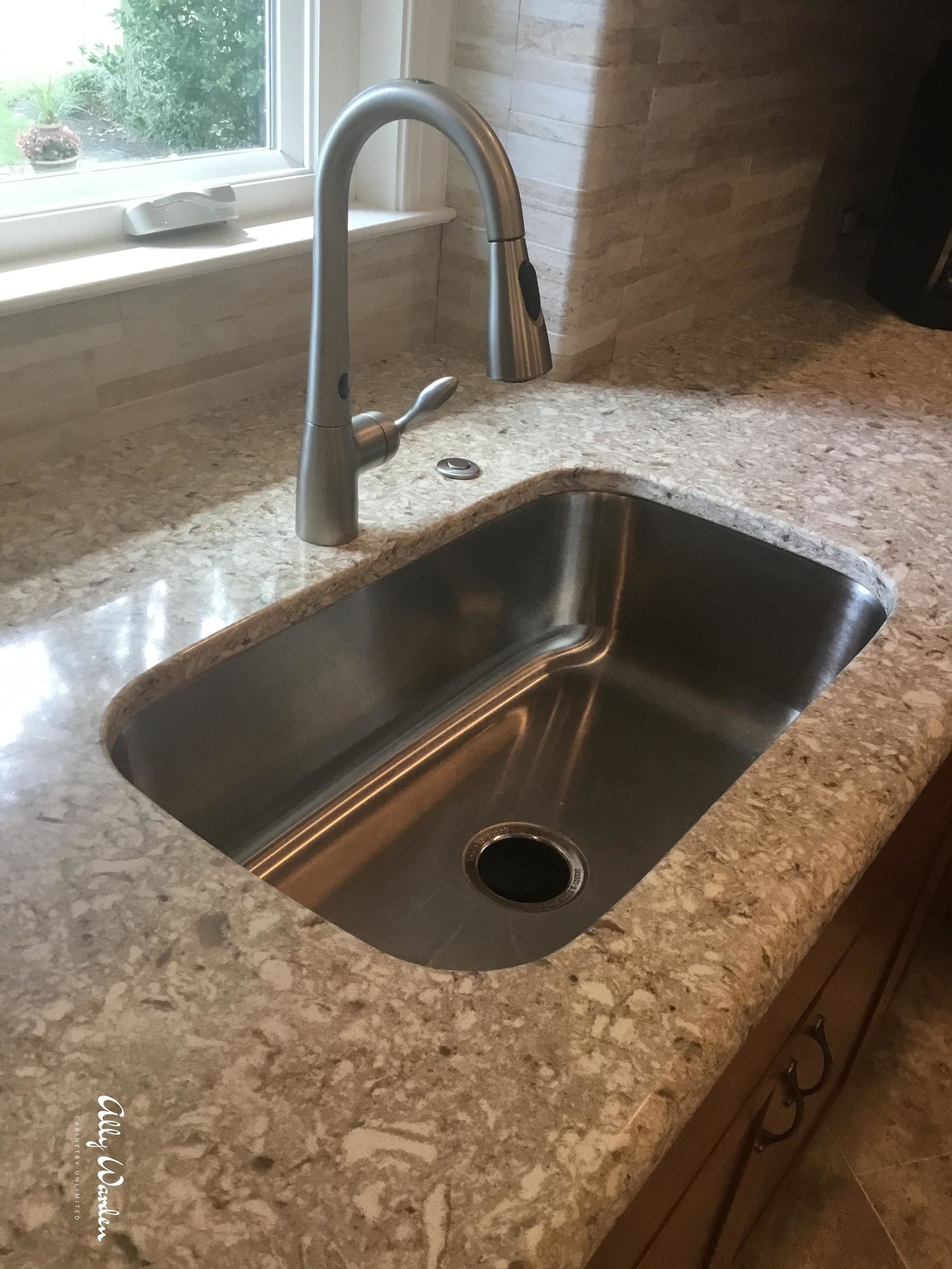 Stainless steel kitchen sink with faucet on a speckled countertop. Window in the background.