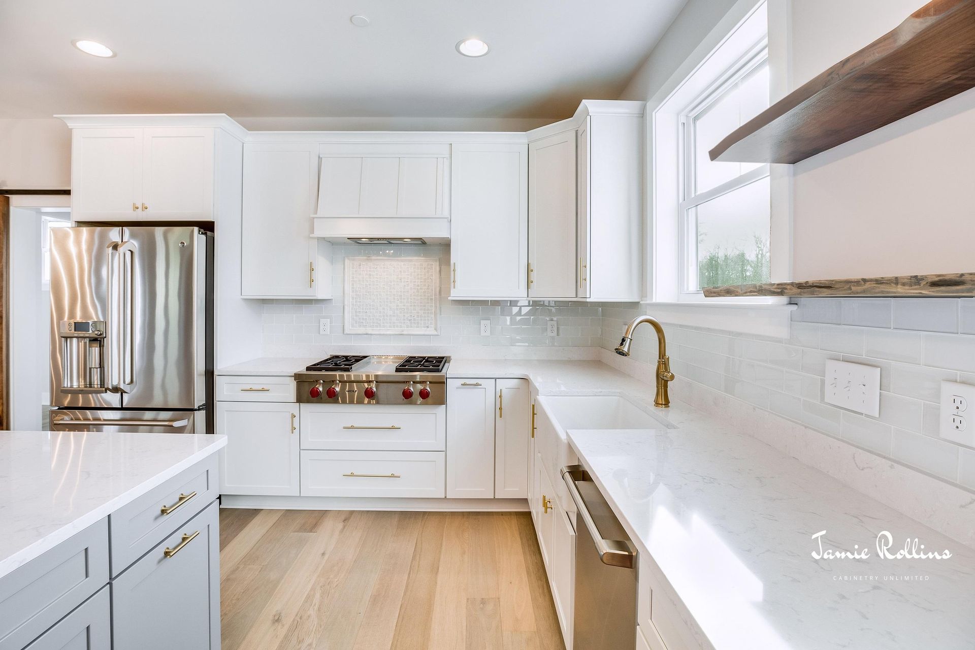 Modern white kitchen with stainless steel appliances, marble countertops, and wooden floors. Features a gas stove and a gray island.
