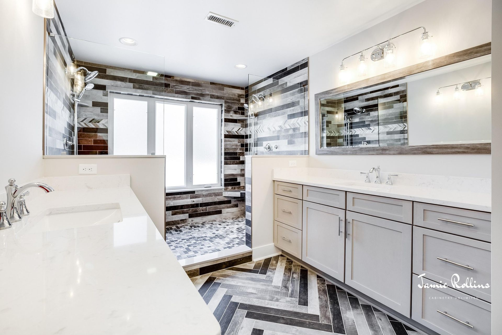 Modern bathroom with herringbone patterned floor, gray cabinets, and a shower with mixed-color tile.