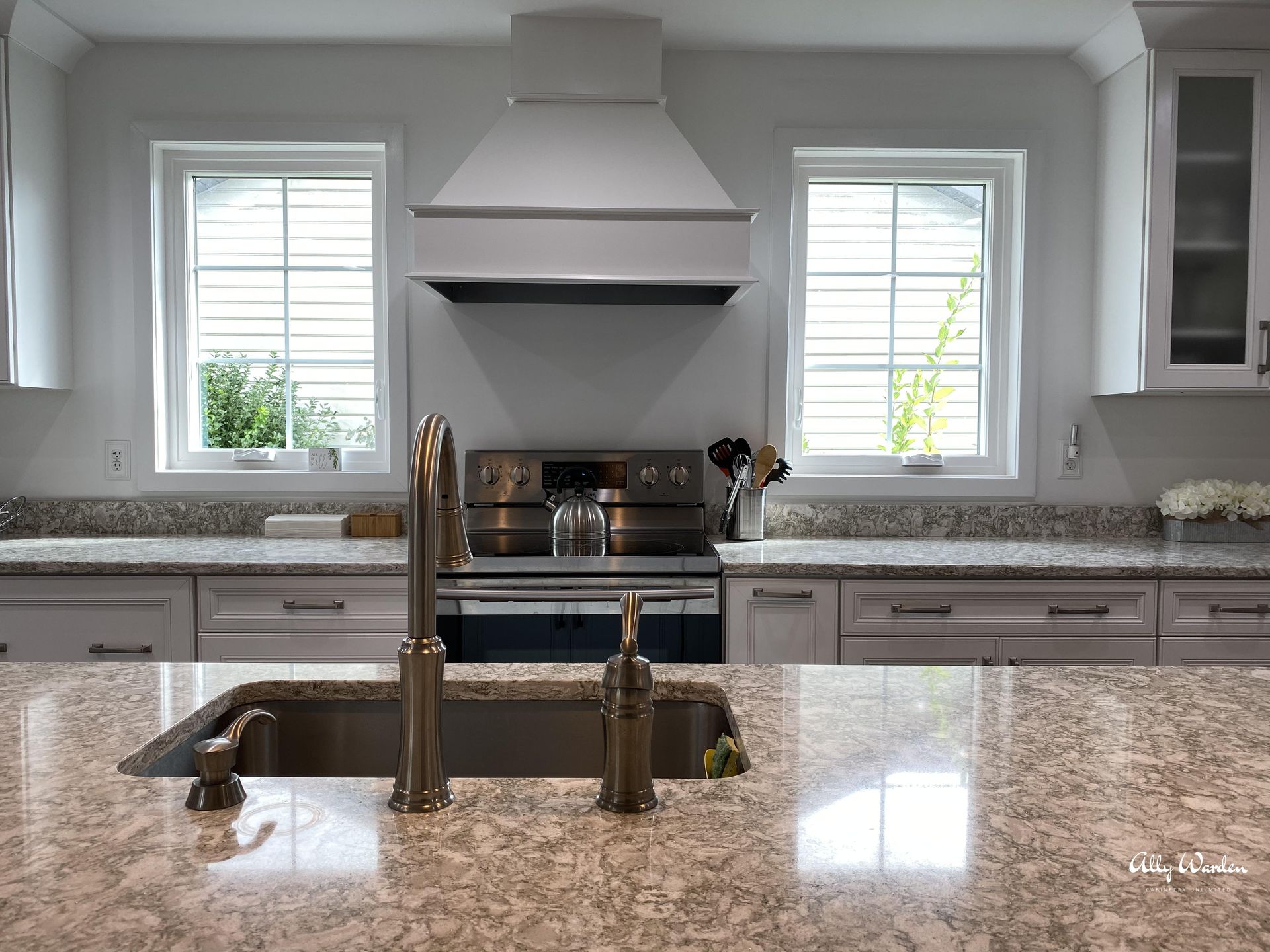 Kitchen with white cabinets, granite countertops, stainless steel appliances, and two windows flanking a range hood.