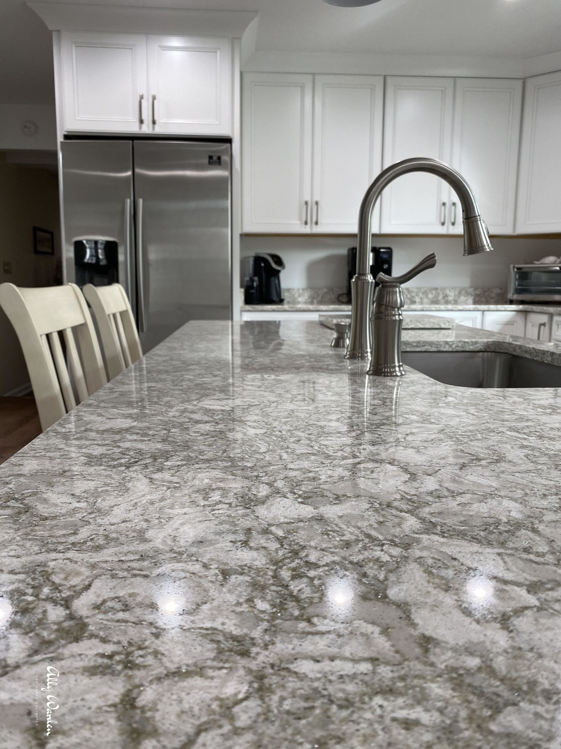 A kitchen island with a gray and white patterned countertop, a stainless steel faucet, and white cabinets.