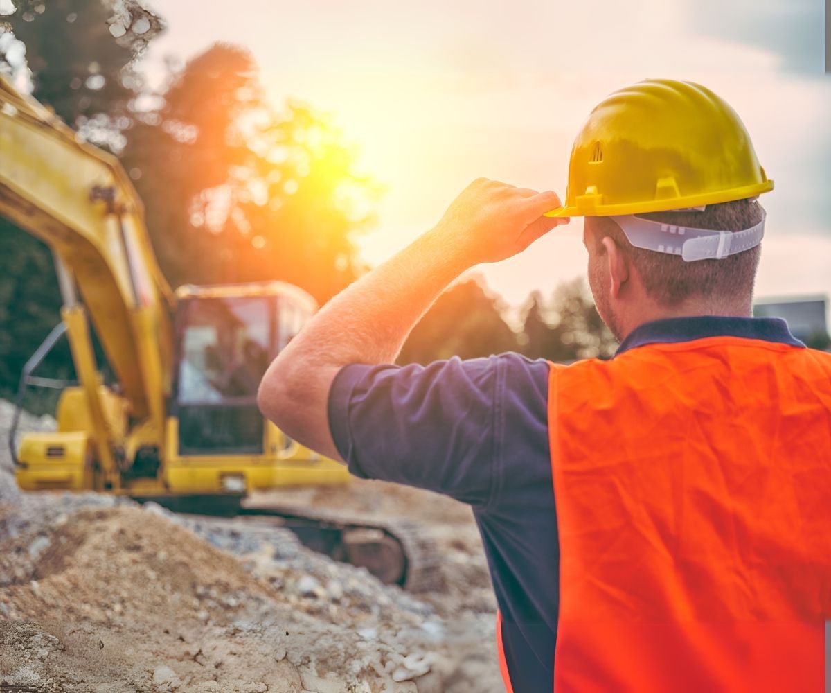 A construction worker wearing a hard hat and orange vest is looking at a bulldozer.