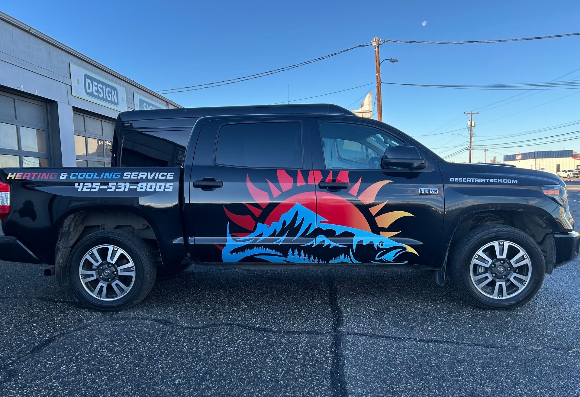 Black Toyota Tundra with mountain and sun graphic, parked in front of a building with a garage door.