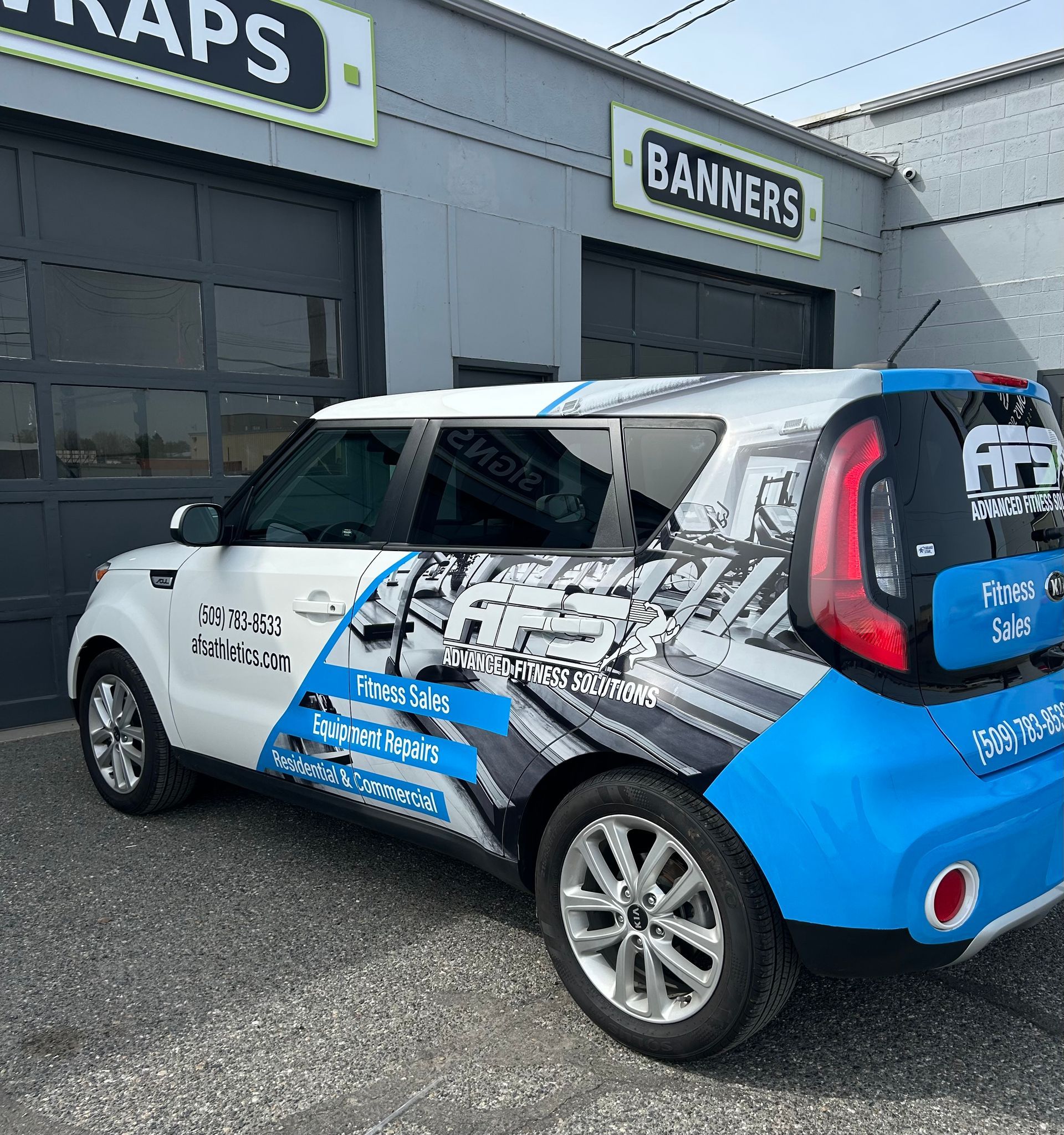 White and blue Kia Soul wrap with company branding parked outside of a building with