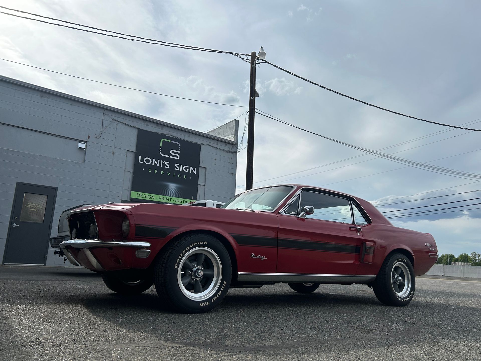 Burgundy 1967 Ford Mustang in front of a gray building under a cloudy sky.