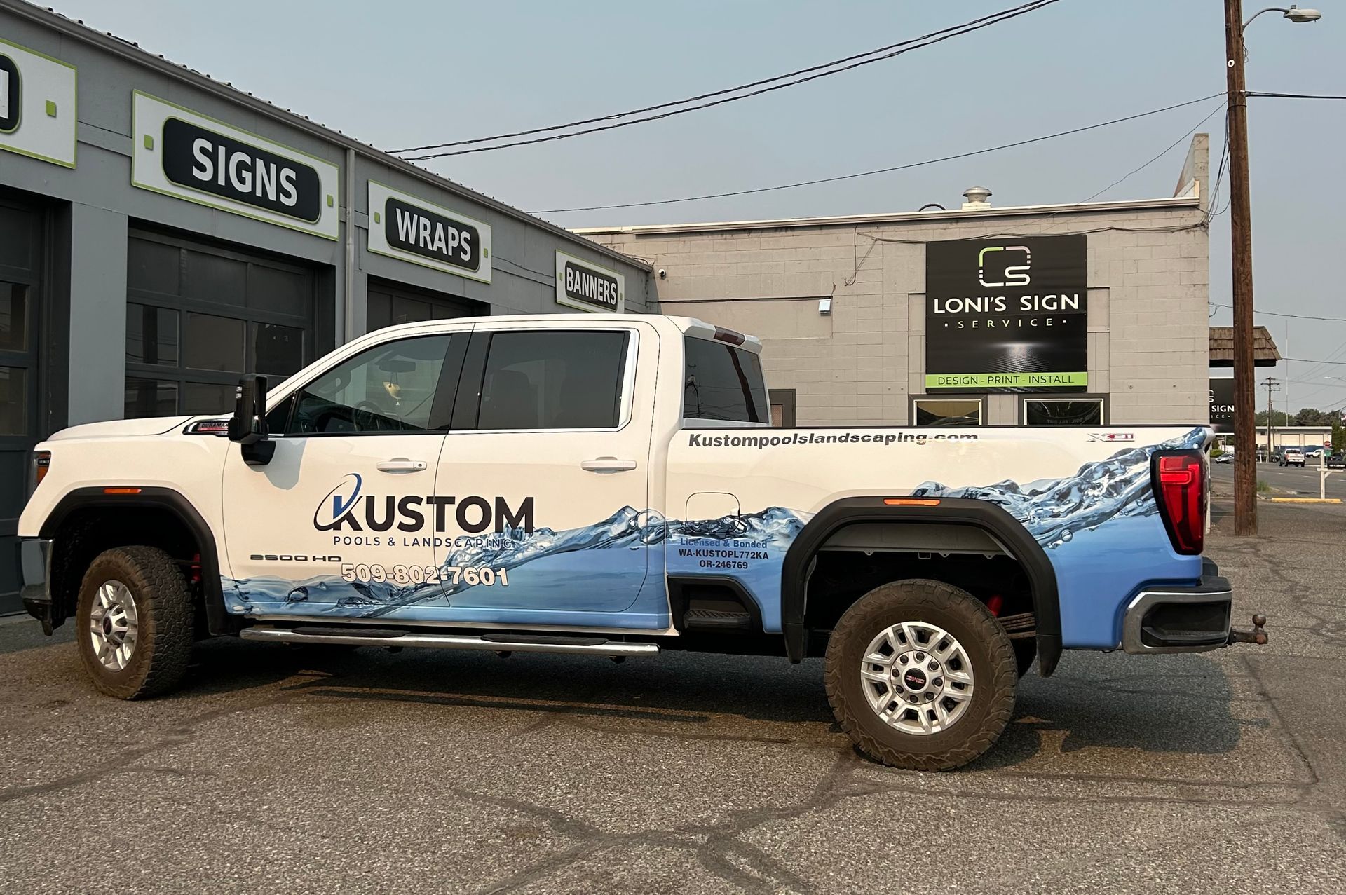 White truck with blue wave graphic parked in front of a sign shop.
