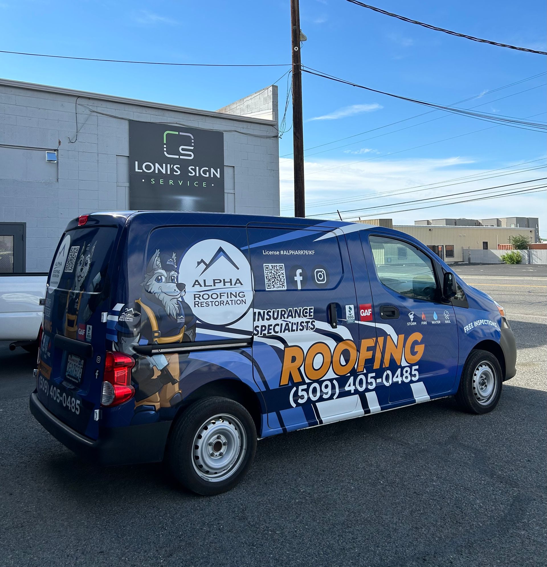 Blue van with roofing company signage parked in front of a building on a sunny day.