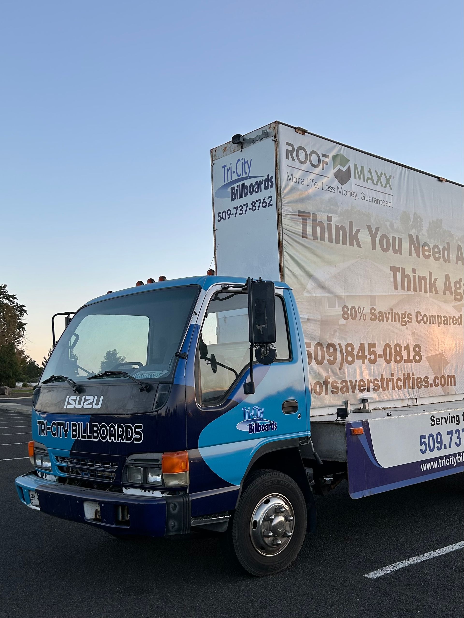Blue and white Isuzu truck, roof and gutter business, parking lot, day.