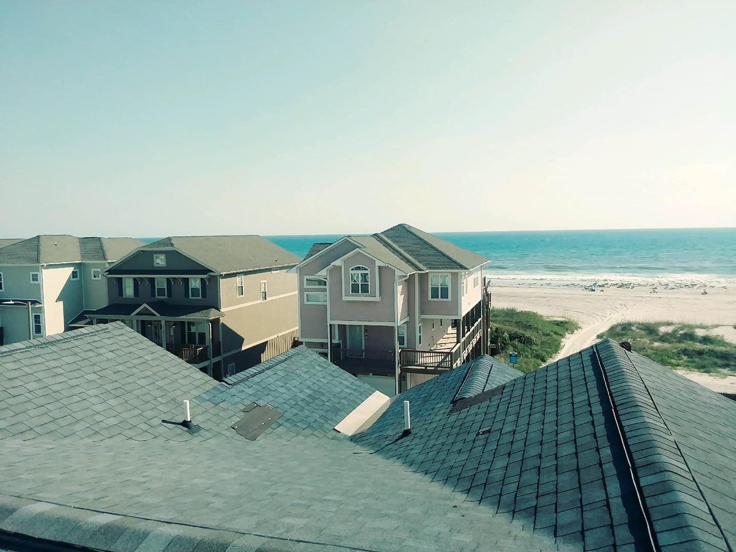 Rooftop view of beach homes, ocean, and sandy beach on a sunny day.