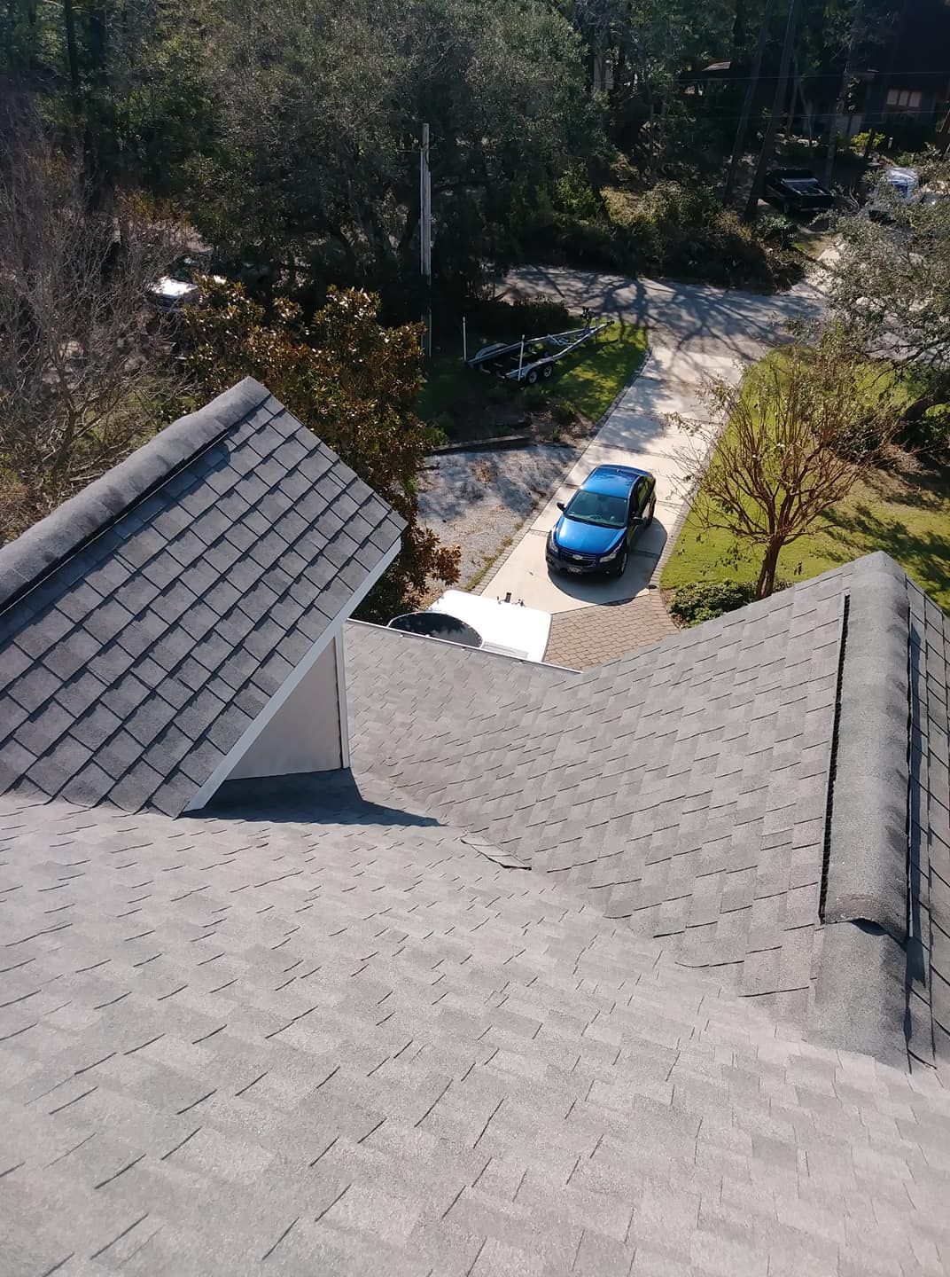Overhead view of a house roof with grey shingles, looking down on a blue car parked in a driveway.