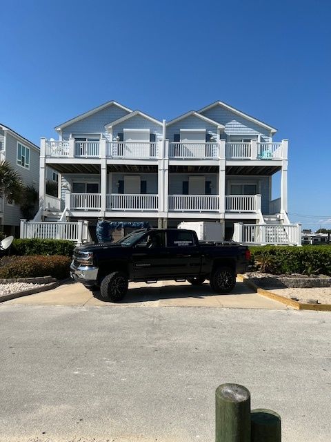 Black truck parked in front of a light blue beach house with white railings on a sunny day.
