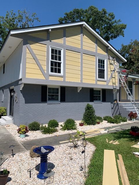 Two-story house with gray, yellow, and white exterior; a person on a ladder working on the house.