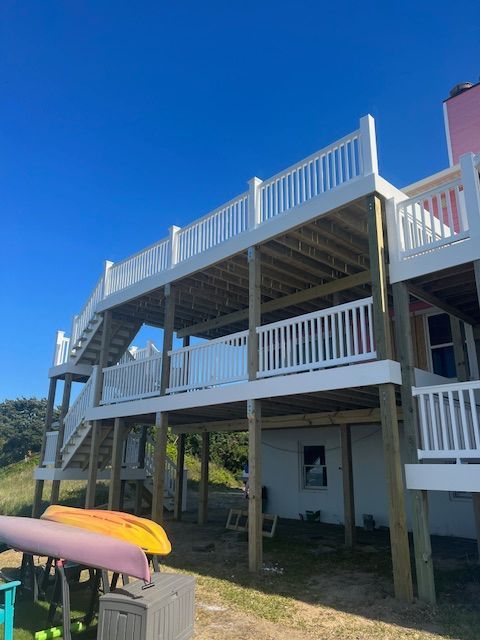 Multi-level deck on a white house with stairs, overlooking grassy area, kayaks in foreground, blue sky.