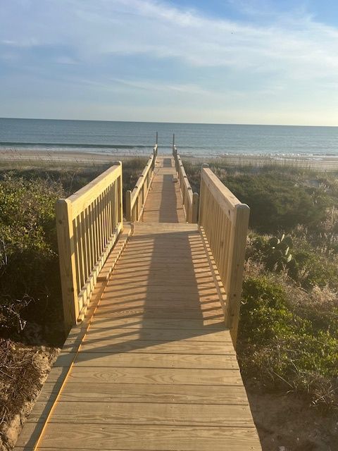 Wooden boardwalk leading to a sandy beach and ocean on a sunny day.