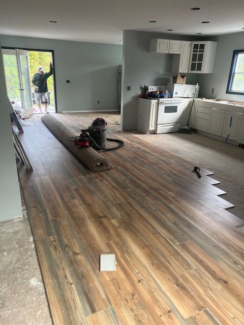Room under renovation; installing wood-look flooring. A person stands in a doorway.