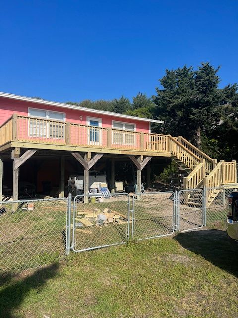 A pink house with a wooden deck, stairs, and a chain-link fence on a sunny day.