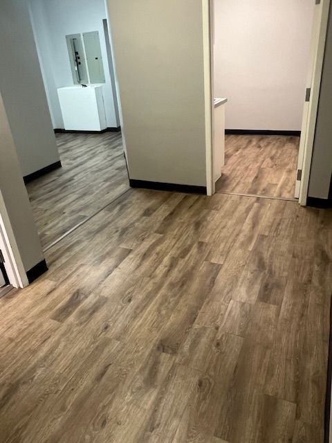 Wood-look flooring in hallway, leading to doorways with white walls. Some electrical equipment visible.