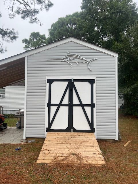 Gray shed with white doors and black accents, a wooden ramp, and a marlin silhouette on the roof.