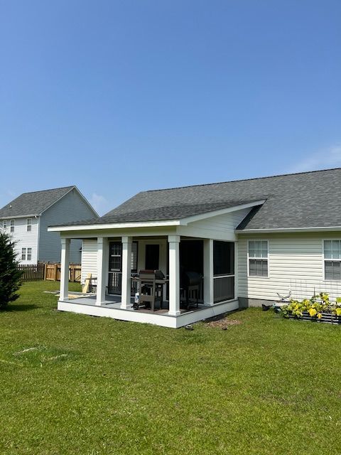 A screened-in porch attached to a white house, with a grill and green lawn under a blue sky.