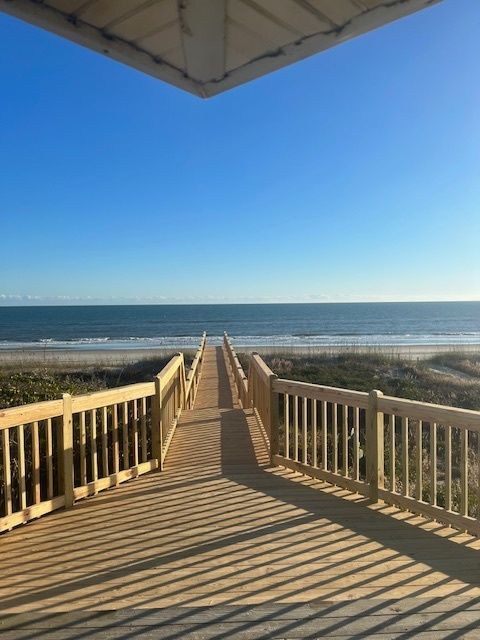 Wooden boardwalk leading to a beach and ocean under a blue sky.