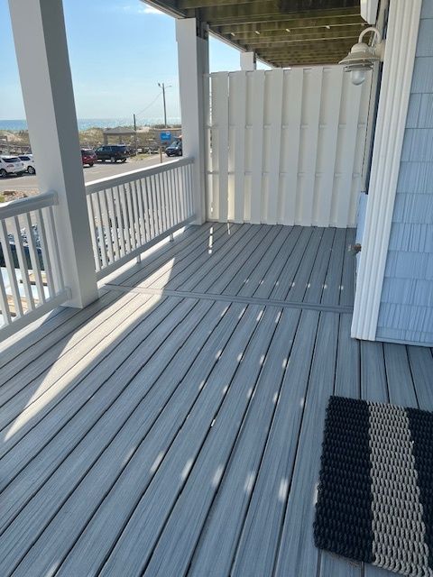 Grey wooden deck with white railing, white siding, and a striped mat. Outdoor setting.