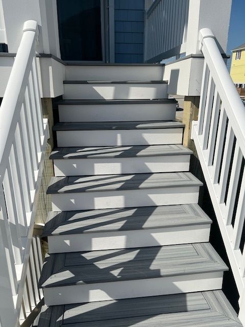 White-railed stairs leading up to a building entrance with gray steps, in an outdoor setting.