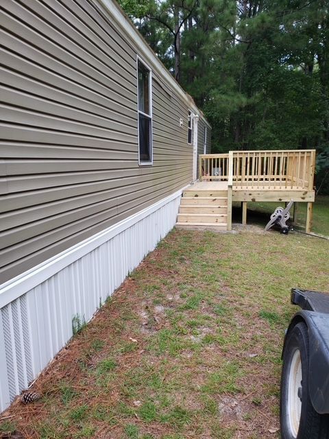 Mobile home with a wooden deck and stairs. Exterior siding is brown with white skirting. Green grass.