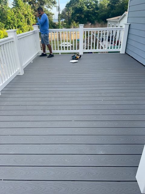 A person on a grey composite deck with white railing. Blue house exterior, sunny day.