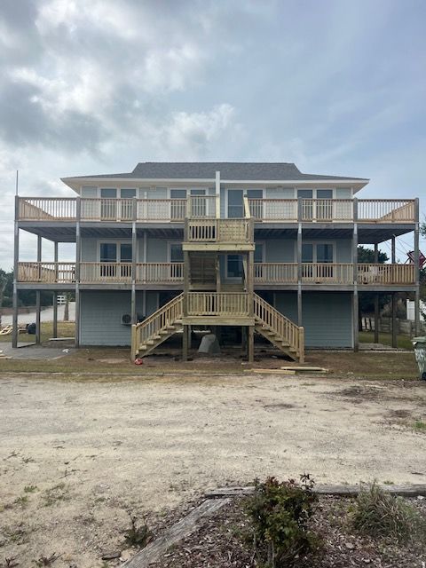 Two-story beach house with wooden decks and stairs under a cloudy sky.