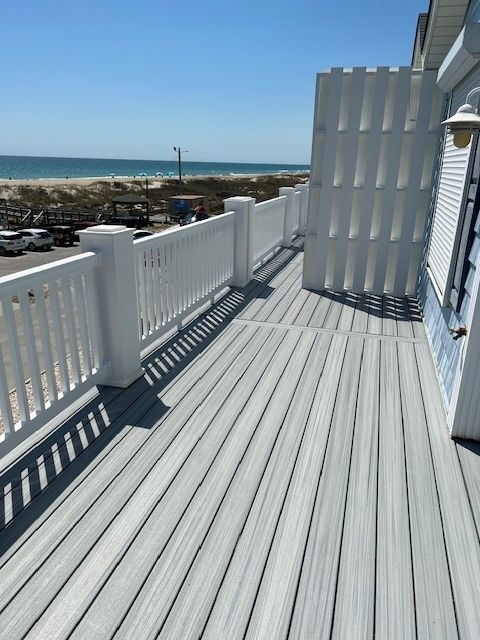 White deck overlooking a beach, with white railing and fence, blue sky.