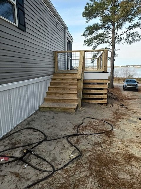 Wooden steps leading up to a deck attached to a light gray mobile home. A water view is in the background.