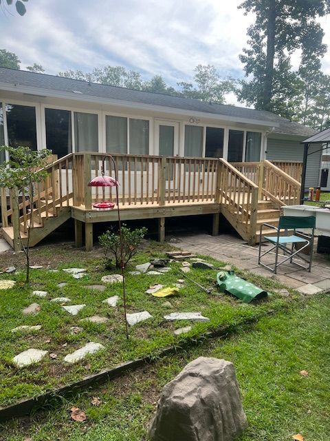 Wooden deck with railings and stairs attached to a house; green yard with stepping stones.