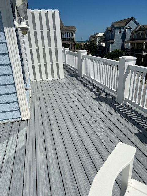 Gray and white deck with railing and vertical privacy screen. Blue siding, sunny day.