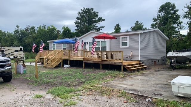 Gray house with wooden deck, American flags, red and blue umbrellas. Boat on trailer nearby.