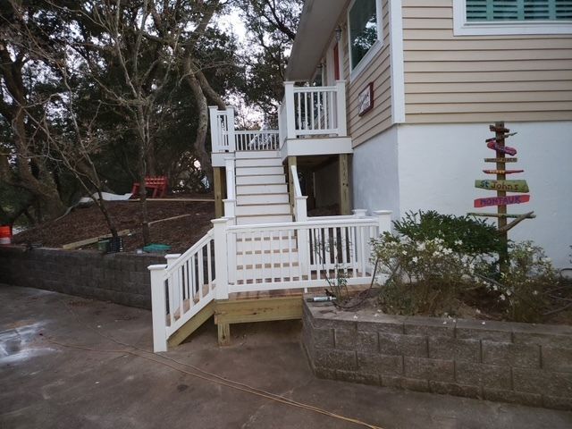White stairs and railings lead up to a light tan house with landscaping.
