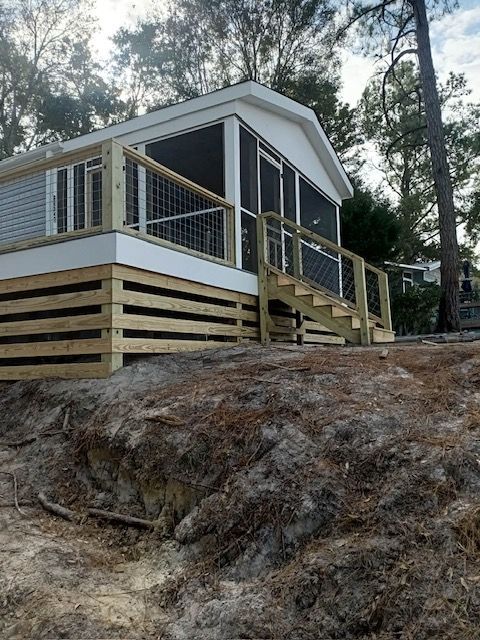 Cabin with screened porch and wooden deck, set on a slightly elevated sandy/dirt terrain.