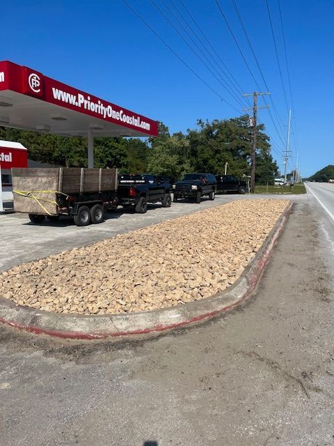 A gas station with a rock-filled median and vehicles parked near a trailer. Blue sky.