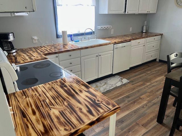 White kitchen cabinets with burnt-wood countertops, white appliances, and wood flooring.