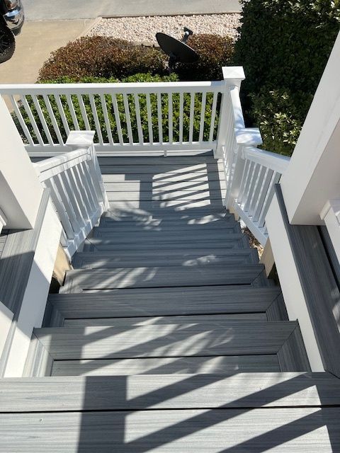 Gray composite stairs with white railing leading down from a deck to a walkway.