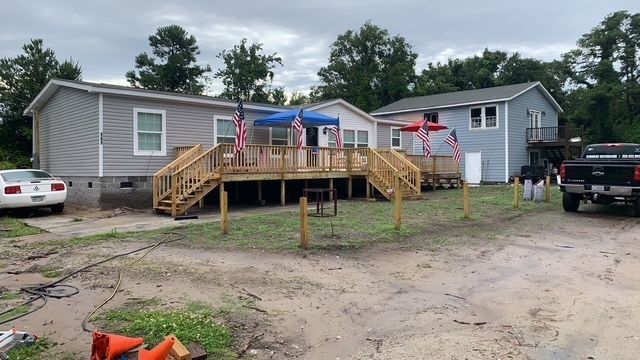 A gray mobile home and blue house with wooden decks, decorated with American flags.