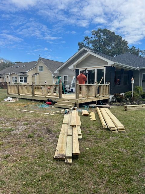 Construction of a wooden deck, lumber and tools on grass in a backyard, with a person working on the deck.