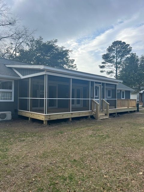 A house with a screened porch and wooden deck in a yard with brown grass under a cloudy sky.