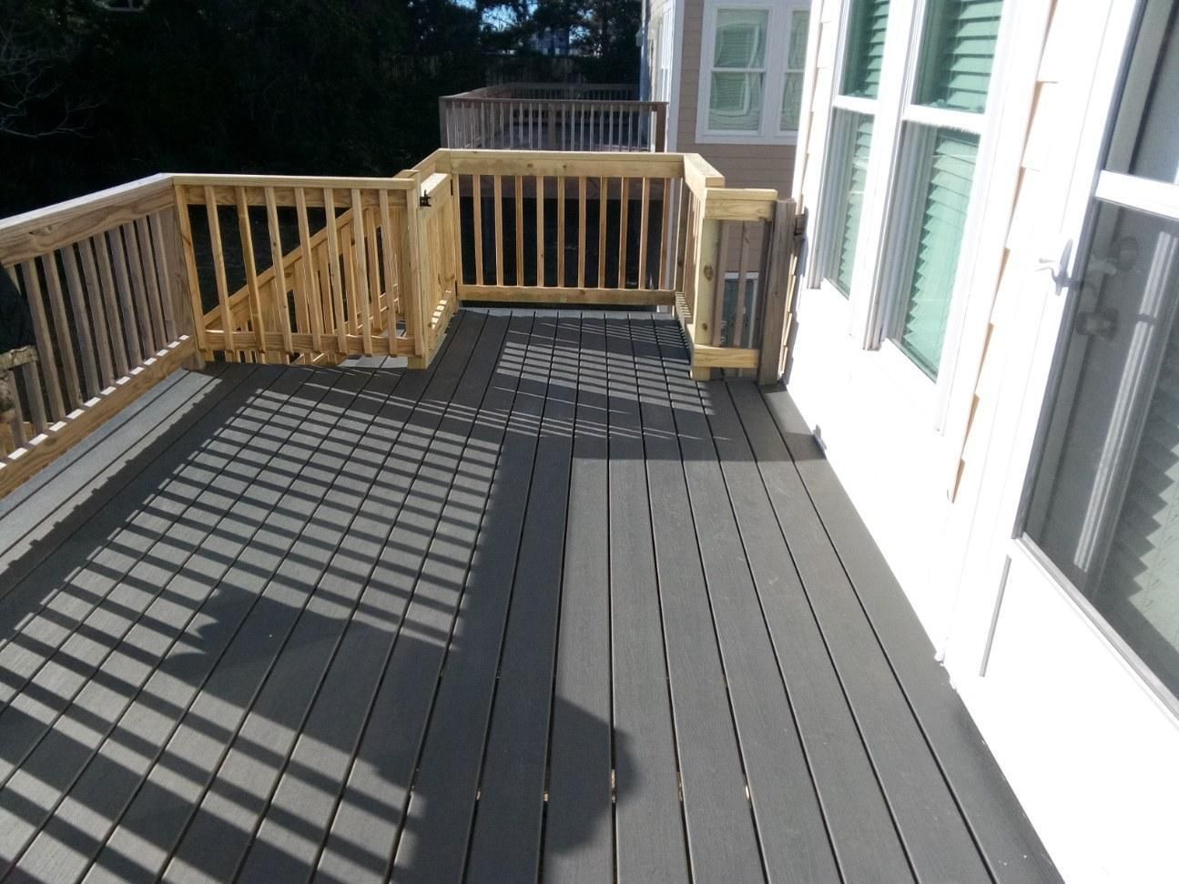 A gray composite deck with wooden railings next to a white house. Sunlight creates shadows.