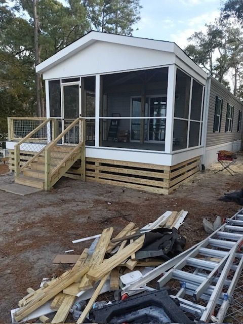 A manufactured home with a screened porch under construction. Wood deck and stairs, debris in the foreground.