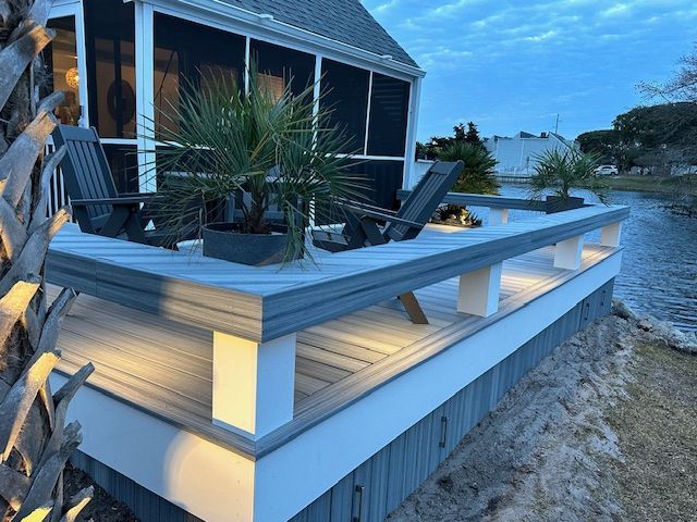 A deck with gray and white trim, chairs, and potted plants overlooking water at dusk.