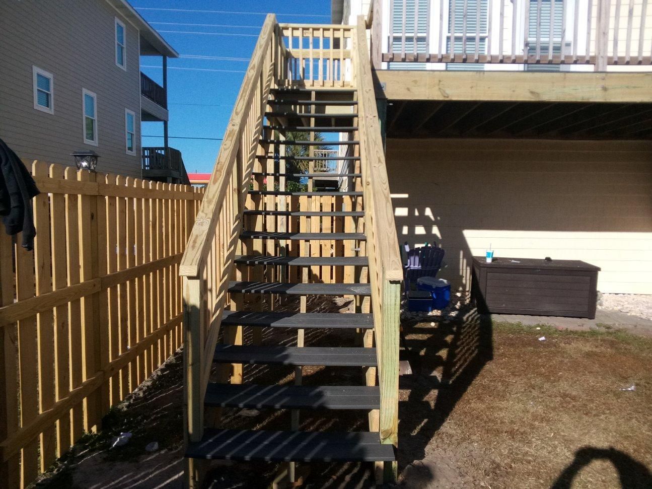 Wooden staircase leading to a deck, next to a wooden fence.