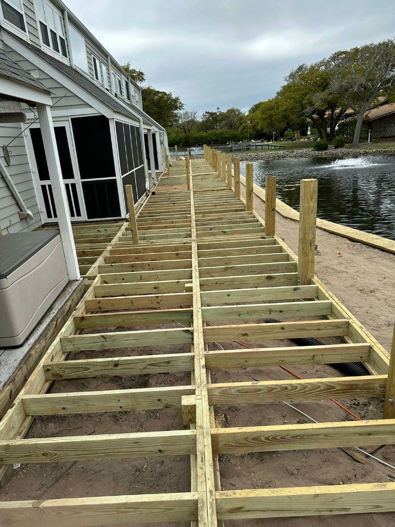 Wooden deck framework being built next to a building and water feature, outdoors.