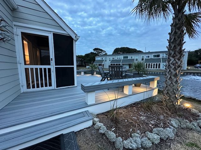 Outdoor deck with water view, dusk. Gray composite decking, bench, palm tree, and buildings.