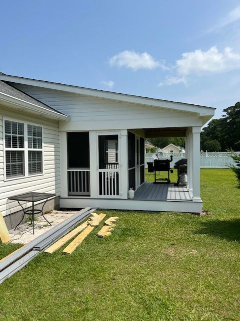 White screened-in porch attached to a house. Grassy yard with building materials.